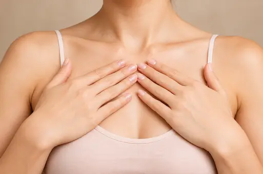 Femme portant un débardeur rose, les mains posées sur la poitrine, illustrant la chirurgie mammaire